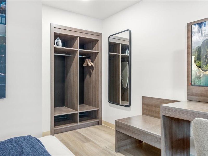 Modern bedroom with open closet, bench, mirror, and light wood furniture