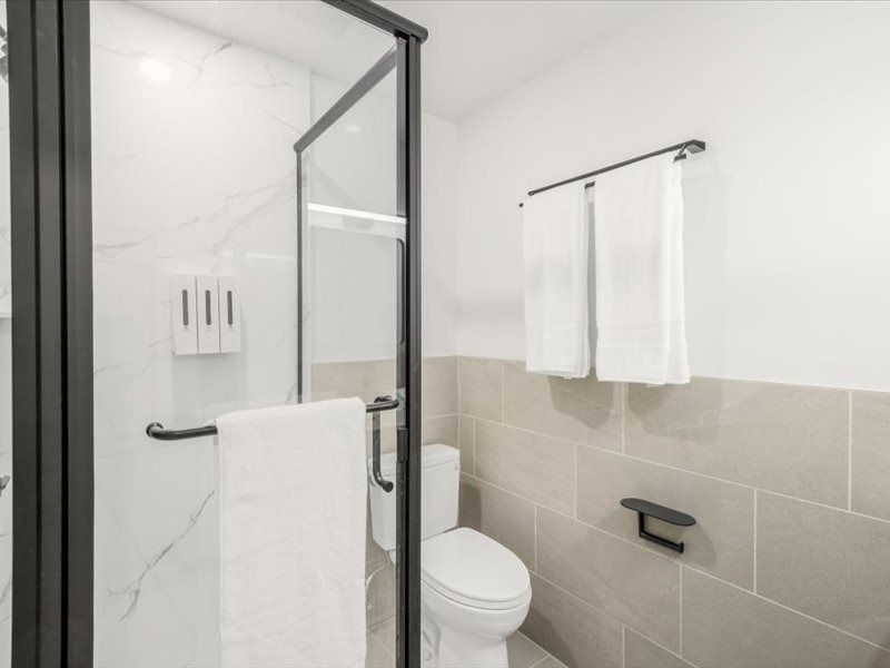 Modern bathroom with glass shower, toilet, beige tile, and white towels on a rack