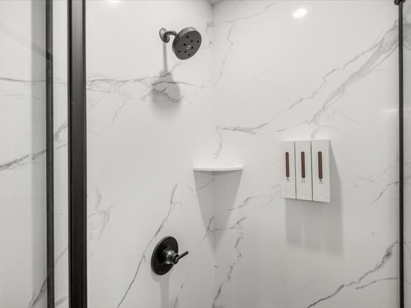 Modern shower with white marble tile, black fixtures, and wall-mounted soap dispensers