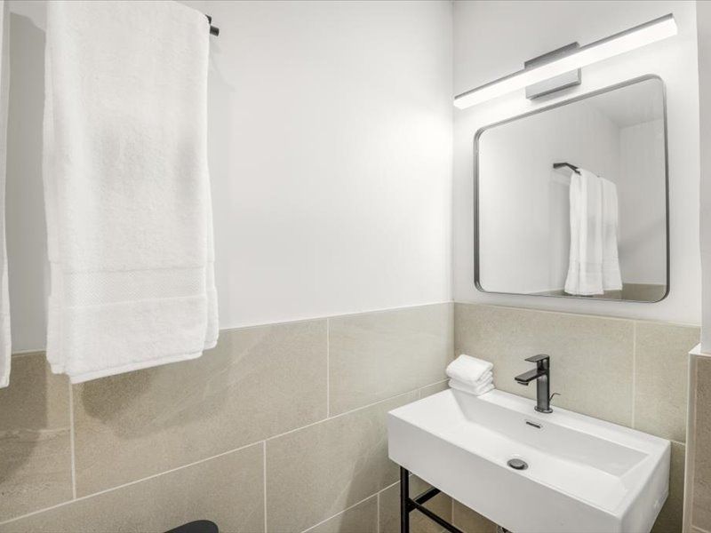 Minimal white bathroom with sink, mirror, towel, and beige tile walls.