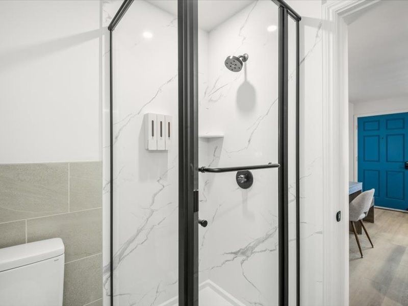 Glass shower enclosure in a white and gray tiled bathroom, with a blue door in the background
