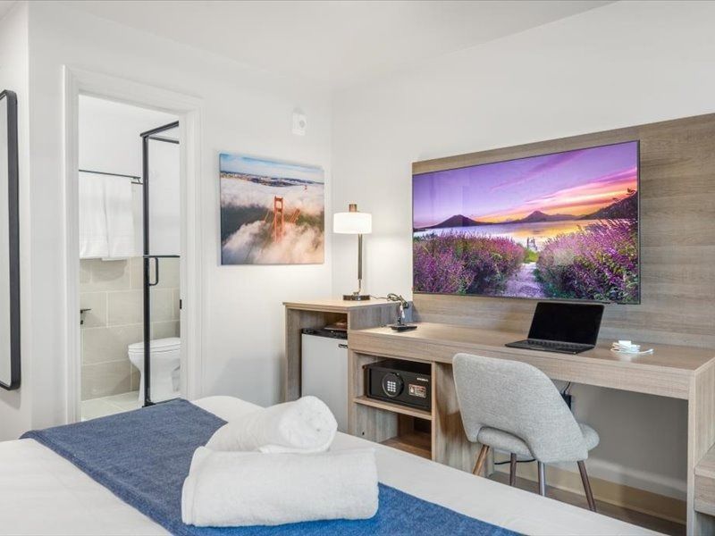 Modern hotel room with twin beds, desk, wall-mounted TV, and bathroom visible through open door