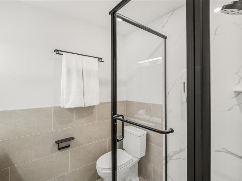 Modern bathroom with a glass shower door, toilet, towel bar, and beige tile walls