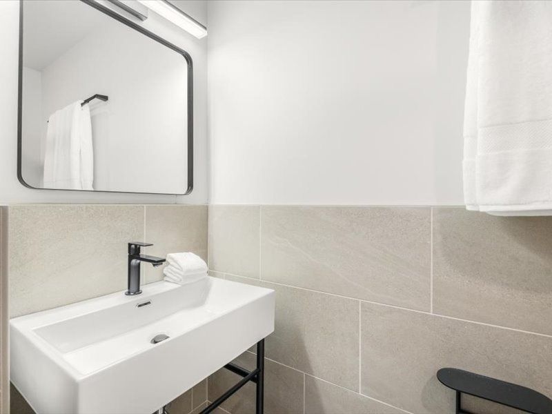 Modern bathroom sink with mirror, beige tile, and black stool.