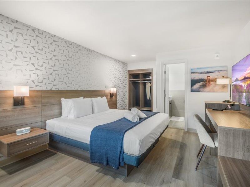 Modern hotel room with a king bed, blue throw, desk, wardrobe, and wall art