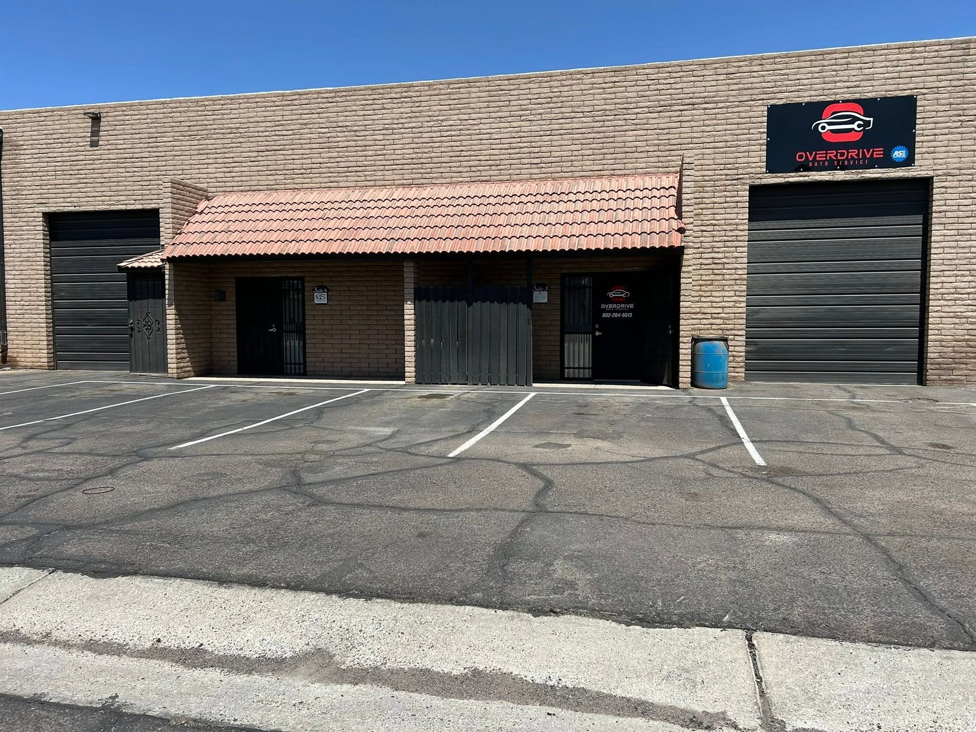Industrial warehouse storefront with brick awning, roll-up doors, and empty parking lot under blue sky | OverDrive Auto Service