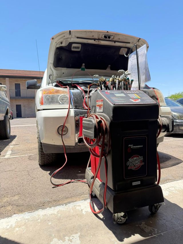 Car engine running with a portable battery charger connected in front of an open hood outdoors | OverDrive Auto Service