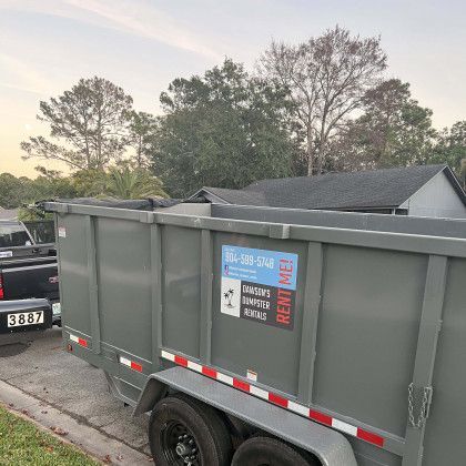 A dumpster is parked on the side of the road next to a truck.