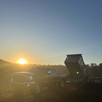 A dump truck is parked in a field at sunset.