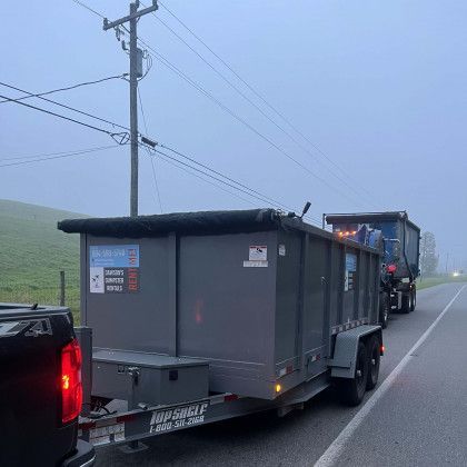 A dumpster is being towed down a road by a truck.