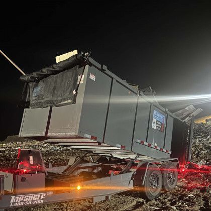 A dumpster is sitting on top of a trailer at night.