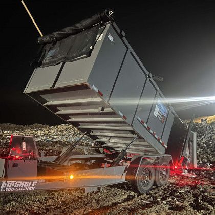 A dumpster is being loaded onto a trailer at night.