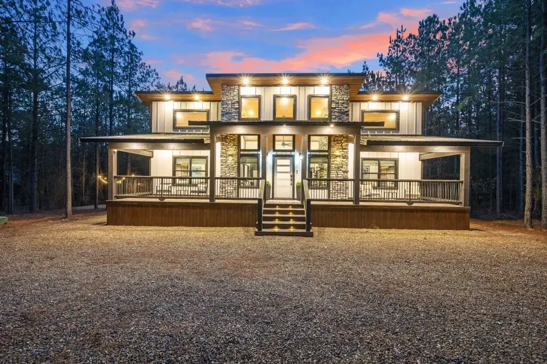 Modern two-story cabin in Broken Bow, Oklahoma with illuminated porch, surrounded by trees, at dusk.