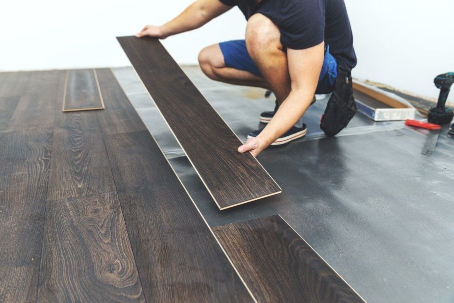 Person installing dark wood flooring on a gray underlayment board