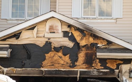 Damaged house exterior with severe fire and smoke charring around the roof and upper facade