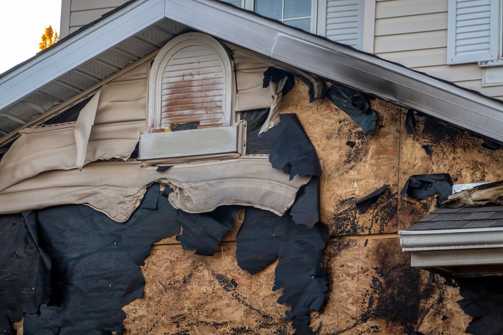 Charred house exterior with melted siding and fire damage beneath a gabled roof