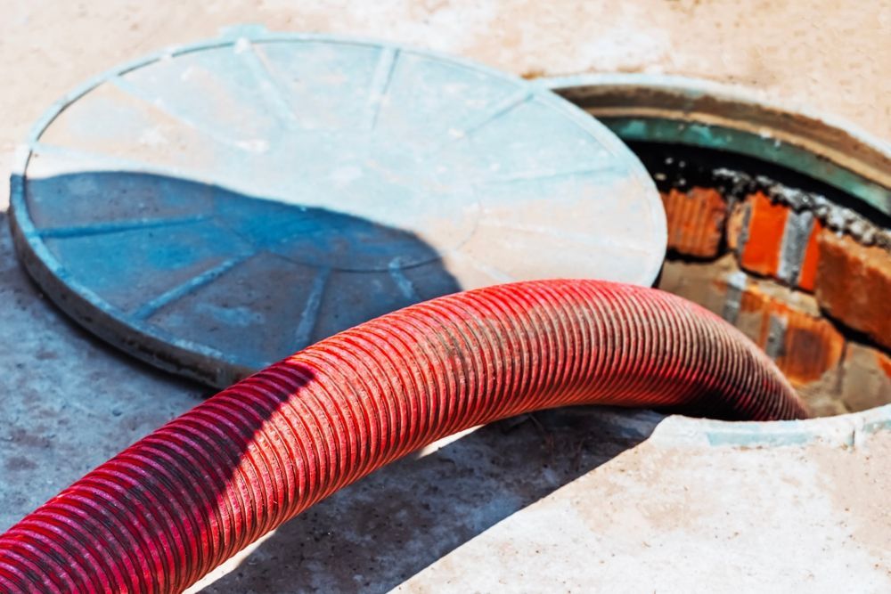 Red hose inserted into a round manhole opening with a metal cover nearby