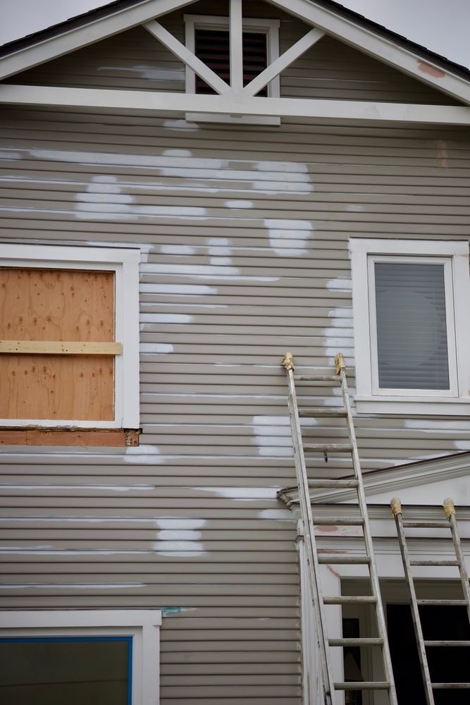 House exterior under repair with beige siding, boarded windows, and ladders leaning against it