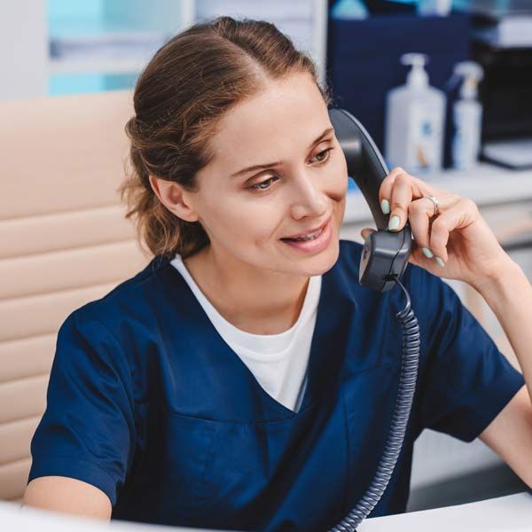 A woman in a blue scrub is talking on the phone to a patient who contacted Victory Medical Institute to Heal and Rejuvenate Your Health with Personalized IV Infusion Treatments, Serving Patients in Morris Plains New Jersey and Manhattan New York