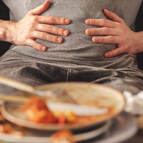 A woman with Hormone Estrogen Dominance has her hands resting on her bloated belly beside a blurred plate of food on a table