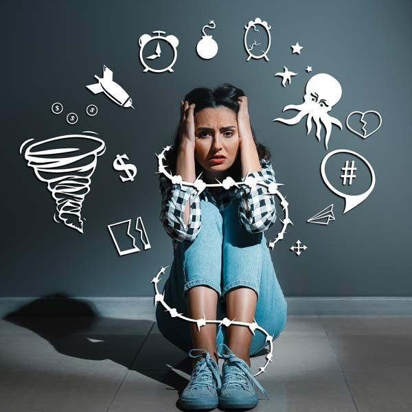 Stressed woman sitting on the floor with hands on her head, surrounded by doodles of worries and symbols
