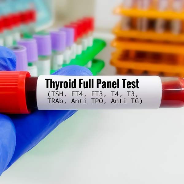 Thyroid full panel test tube held in a gloved hand, with lab racks blurred in the background