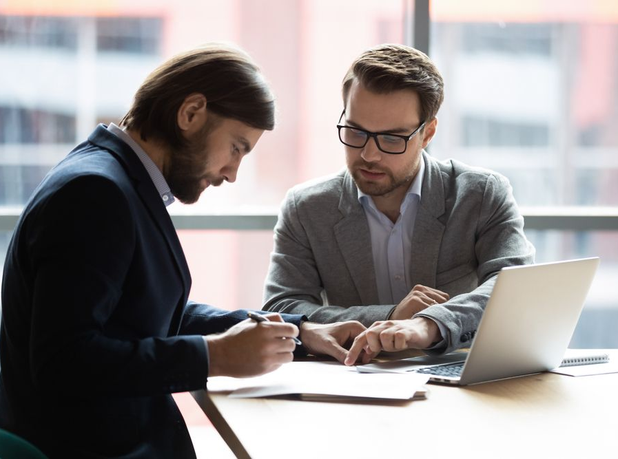 Two coworkers reviewing documents at a table with a laptop in a bright office