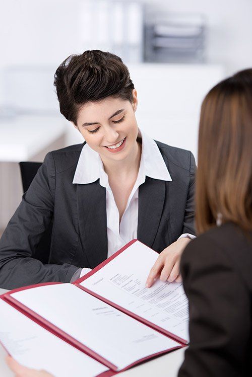 Two people reviewing documents in a bright office, one smiling and pointing at an open folder.