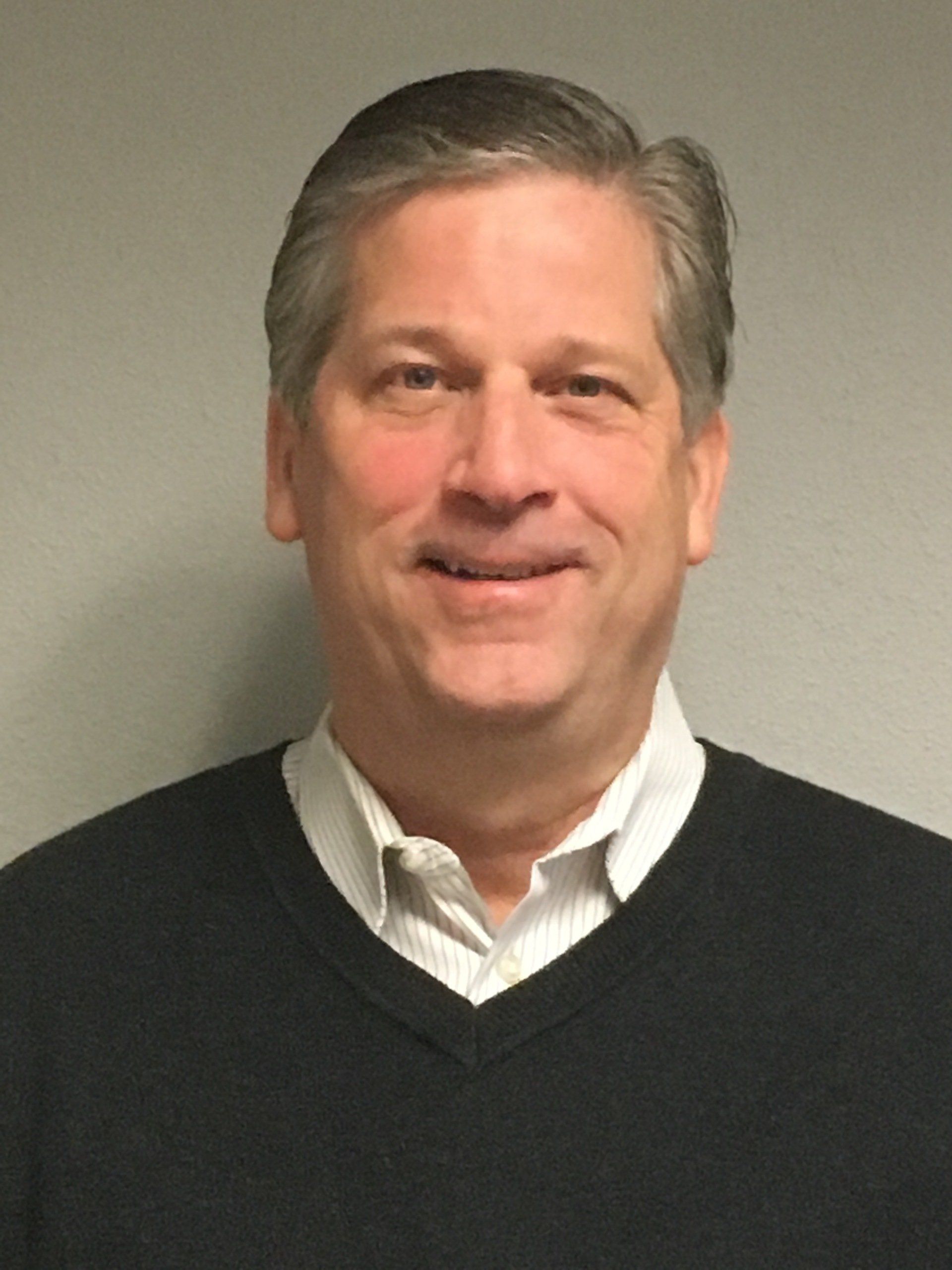 A man wearing a black sweater and a white shirt is smiling for the camera.