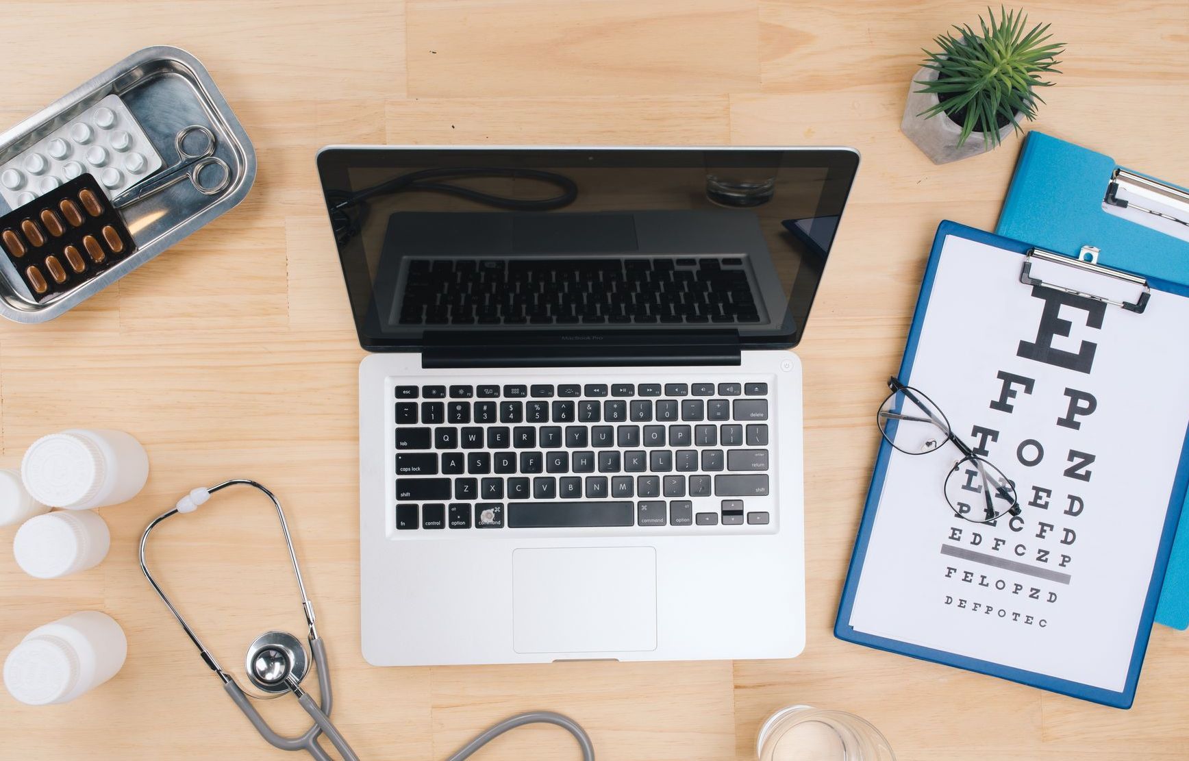 a laptop sits on a wooden desk next to a clipboard with a snellen chart, group vision insurance makes it easy for your top talent to be taken care of