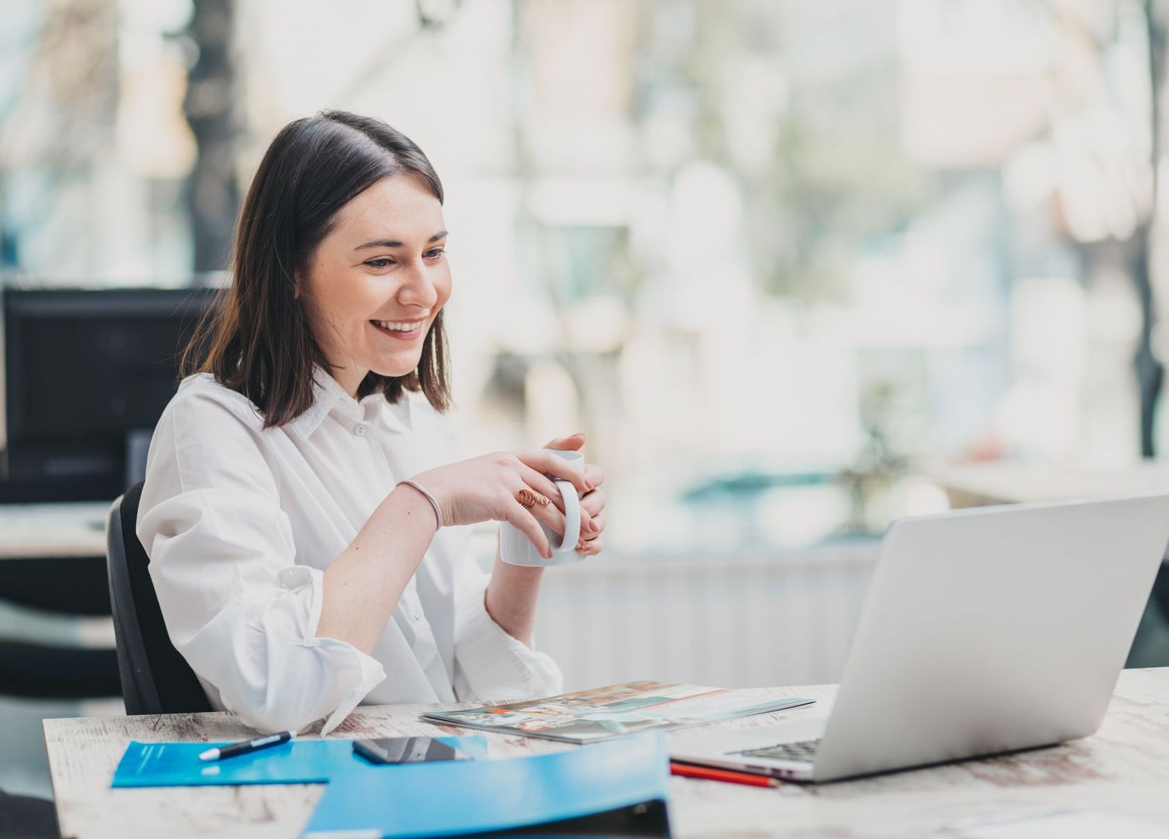an employee benefits broker sits at her desk with a laptop and a cup of coffee