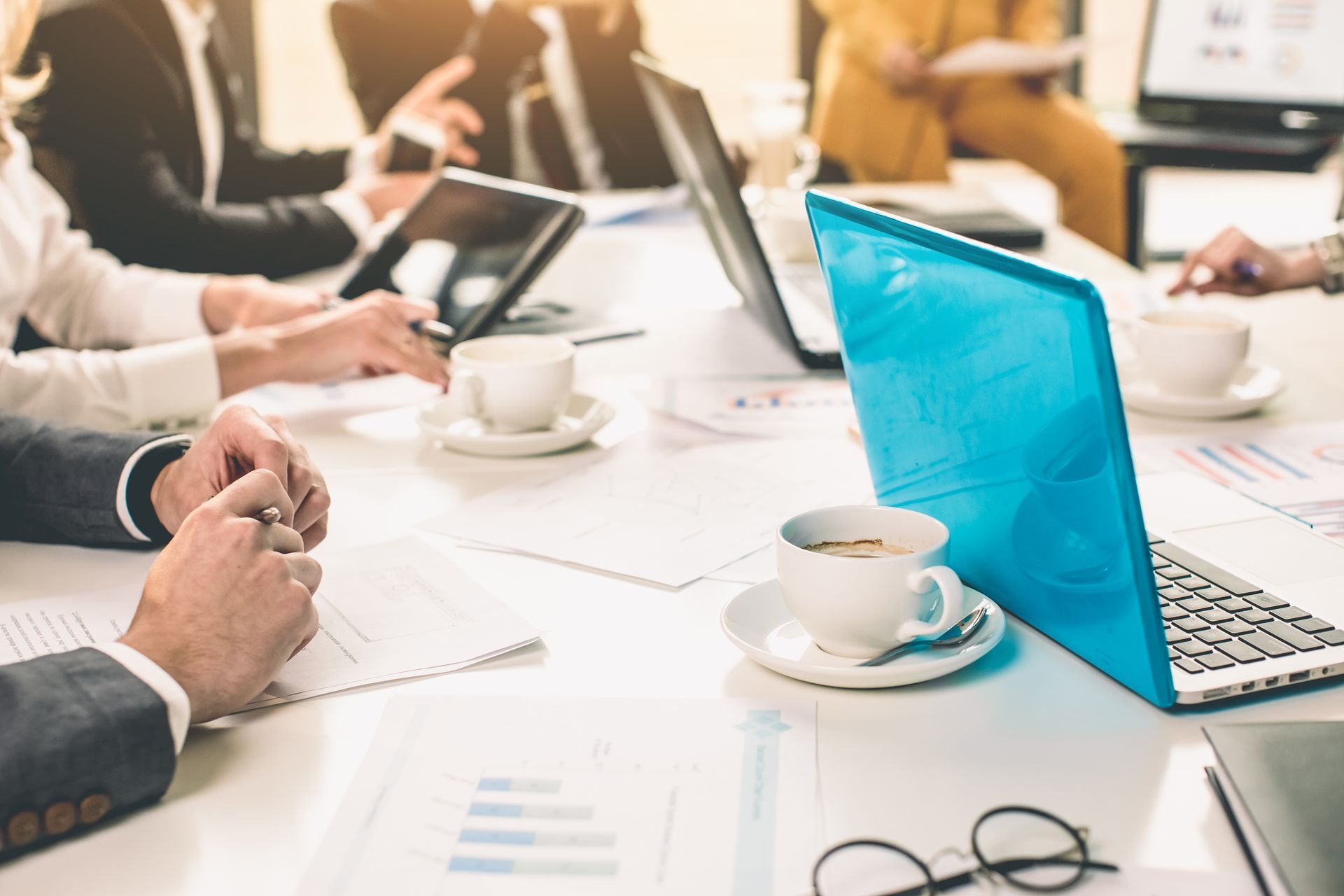 A meeting table with coffee cups, laptops, papers, and other miscellaneous office items