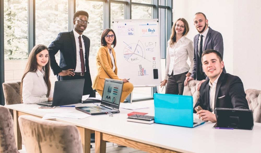 A group of insurance professionals smiles as they gather around a meeting table, discussing buy sell agreements