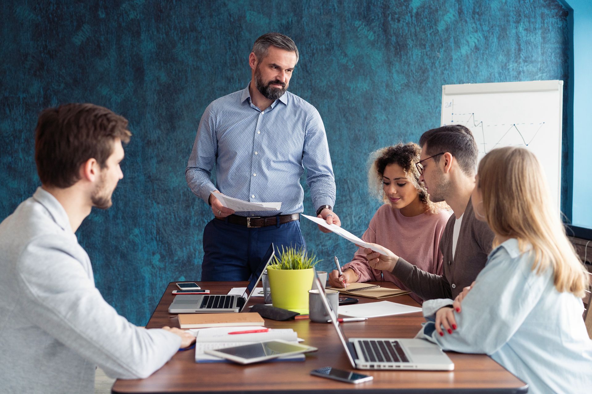 An HR manager is giving a presentation to a group of people sitting around a table about what to keep in personnel files