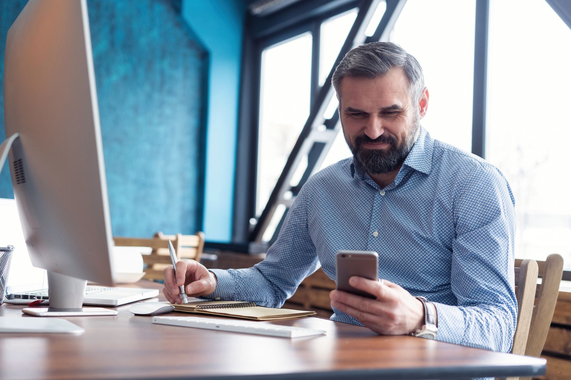 A man is sitting at a desk looking at his cell phone.