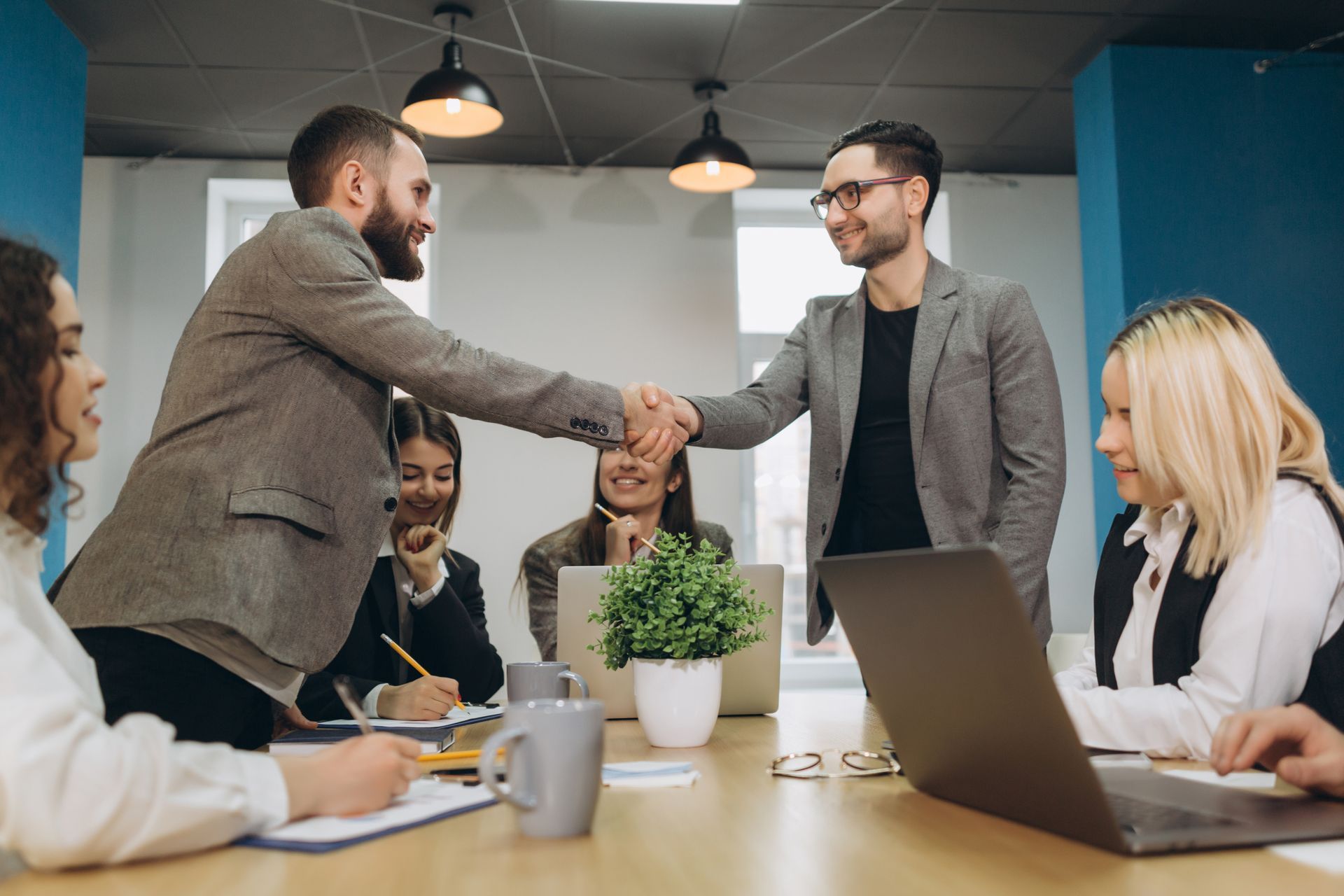 a group of people are sitting around a table shaking hands after meeting to discuss how technology is changing the employee benefits landscape