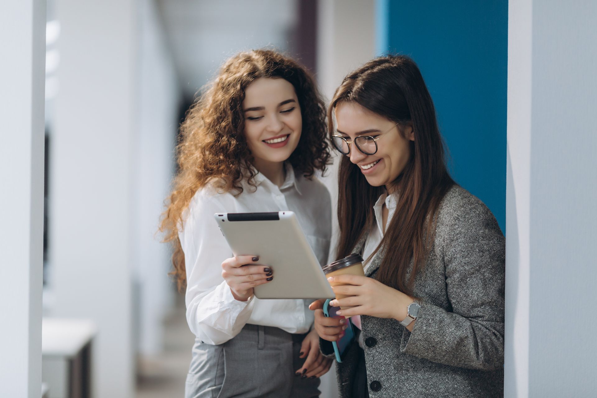 two women are looking at a tablet together in a hallway exploring employee health benefits