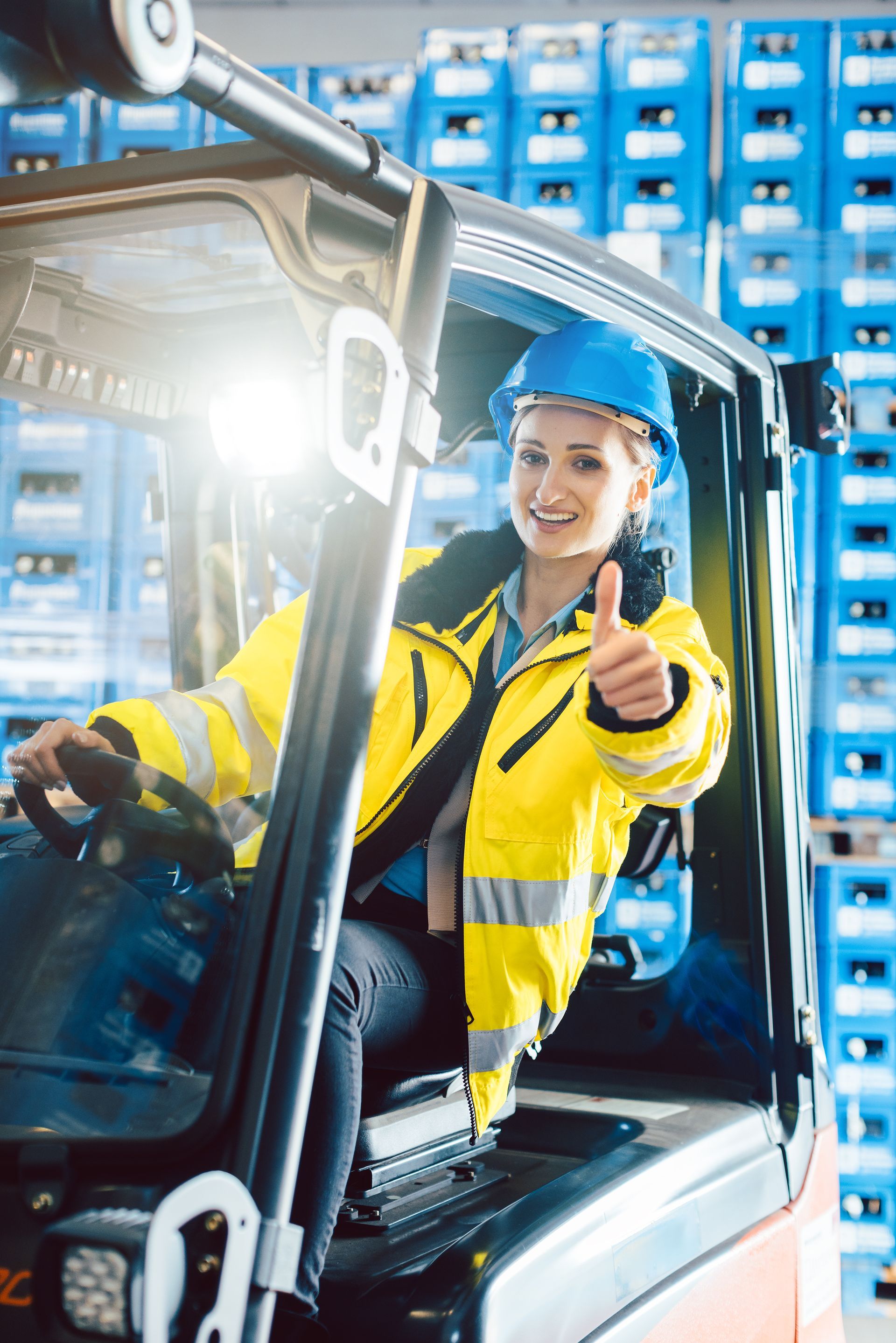 A woman is sitting in a forklift and giving a thumbs up.
