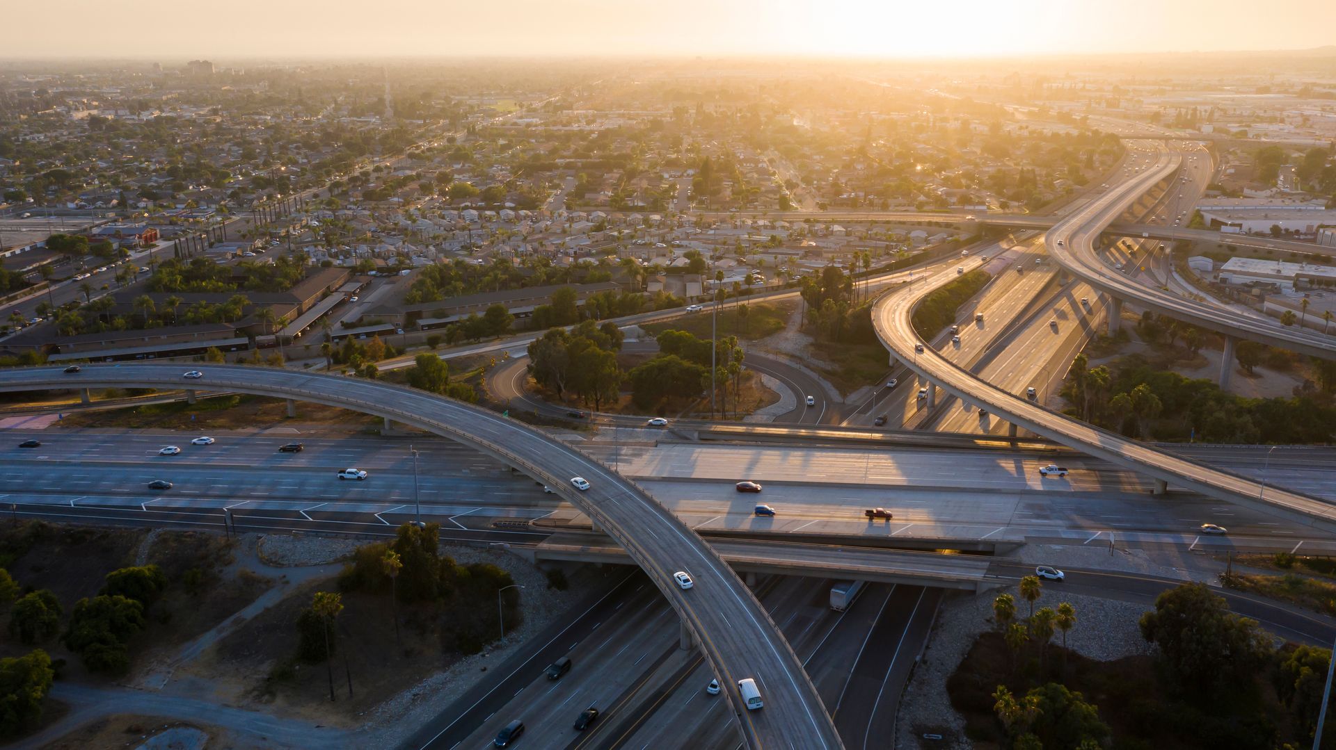Sunset over a sprawling highway interchange with cars and long shadows across the city.