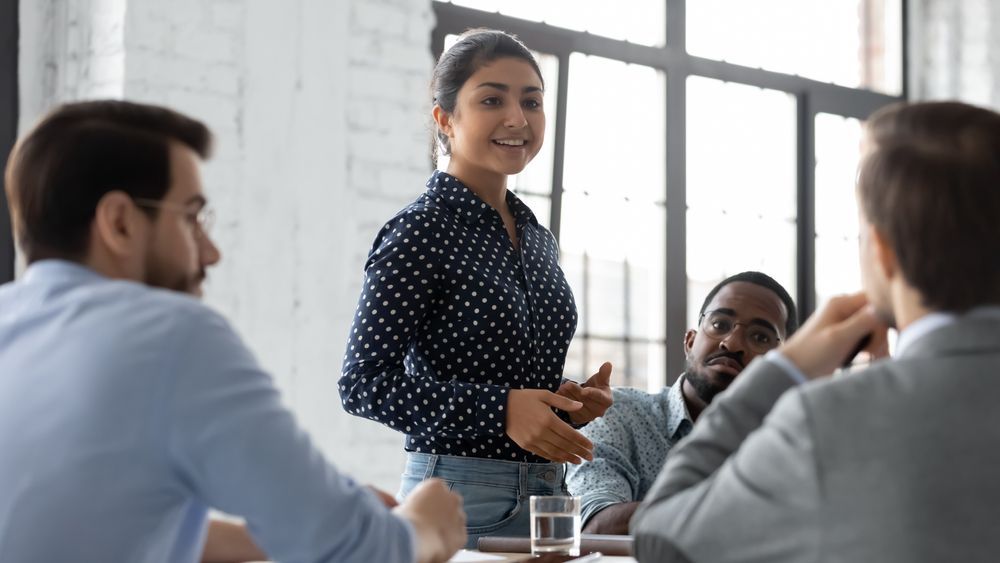 A woman is giving a presentation to a group of people sitting around a table.