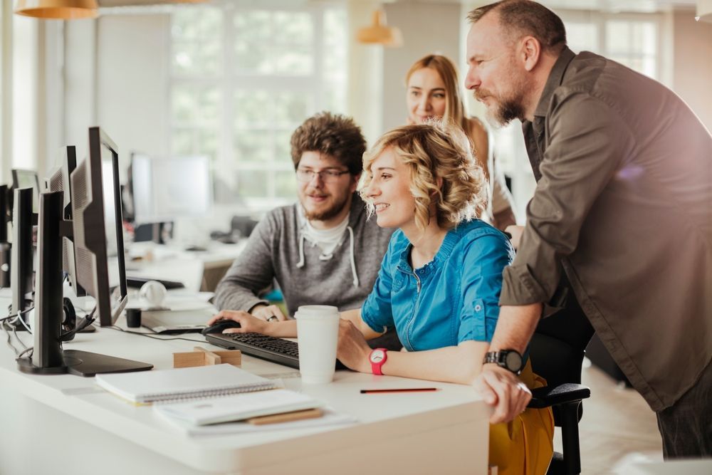 A group of people are looking at a computer screen in an office.