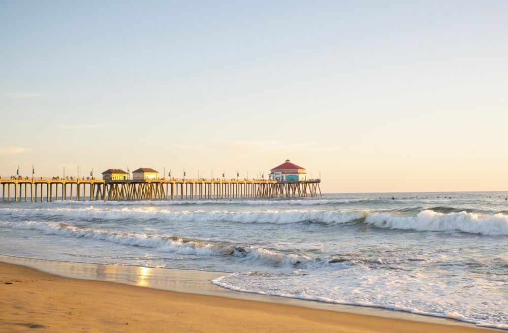 Sandy beach with waves and a long pier at sunset