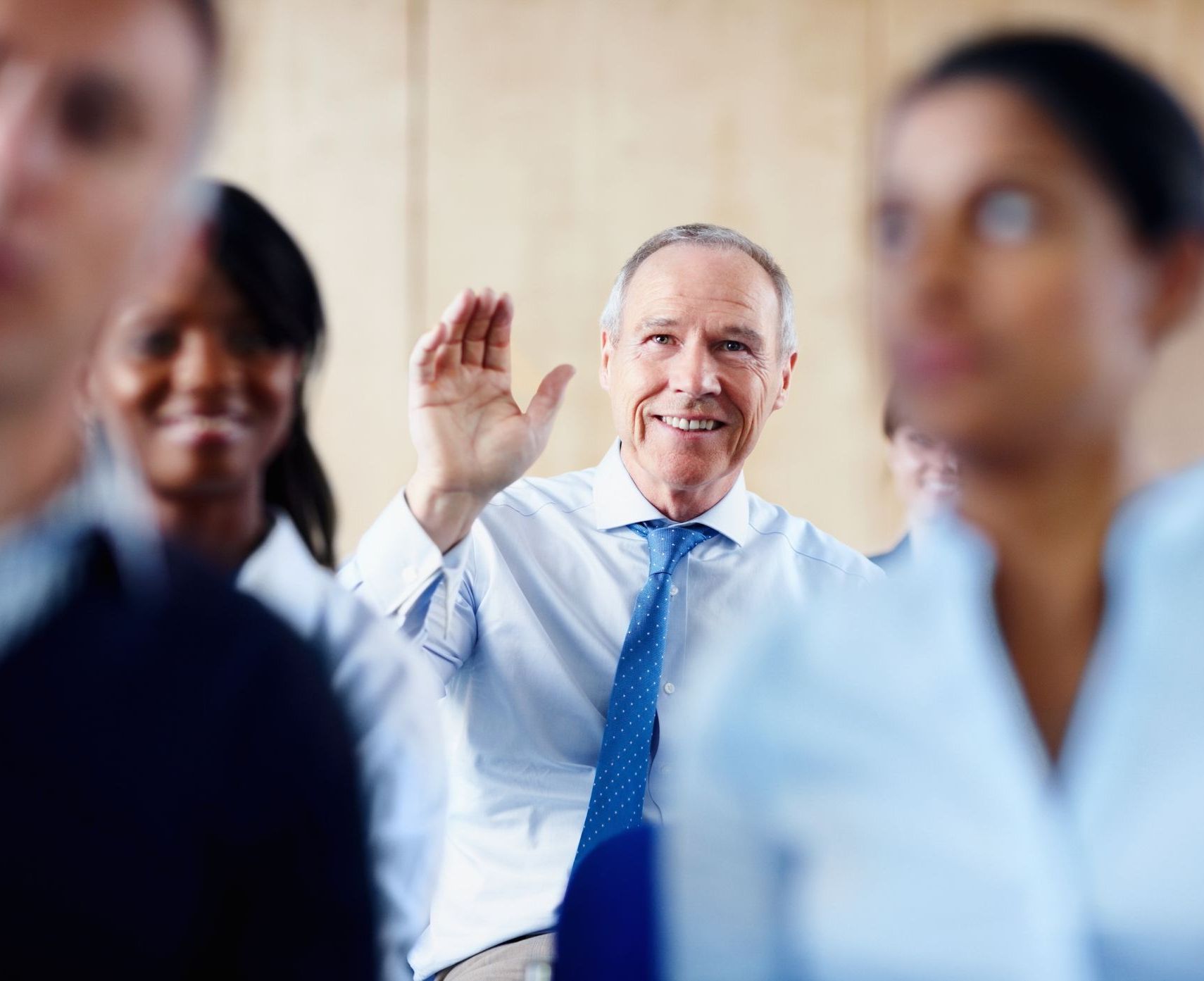 A group of people are sitting in a room and one of them is waving.