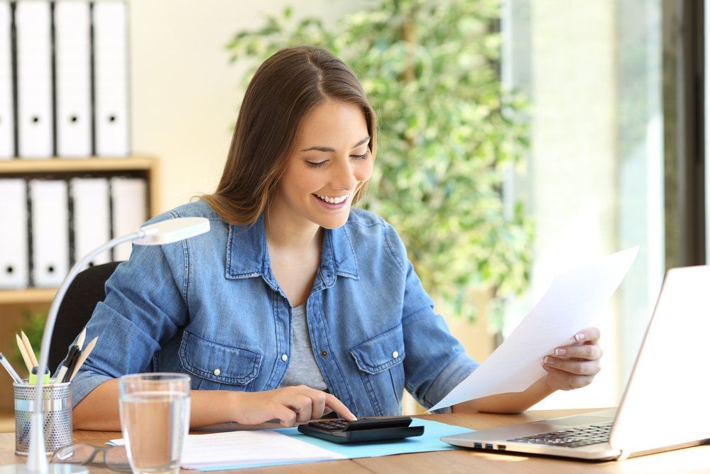 A woman is sitting at a desk with a laptop and a calculator.