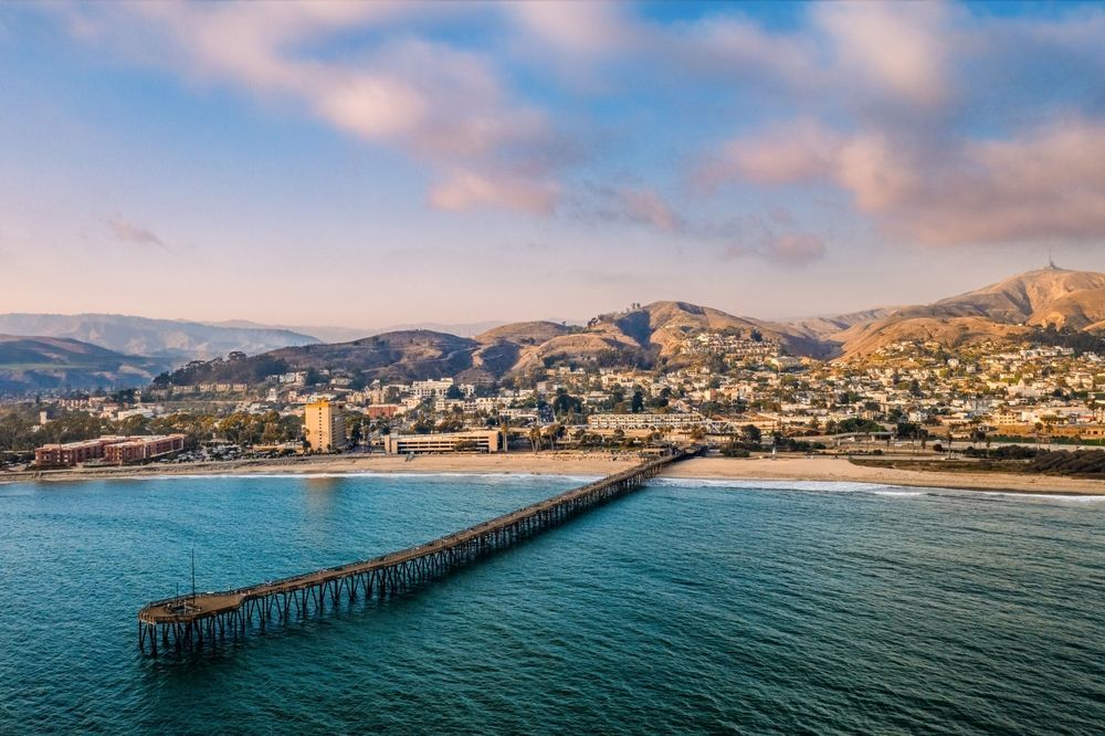 Aerial view of a coastal city with a long pier stretching into turquoise water at sunset