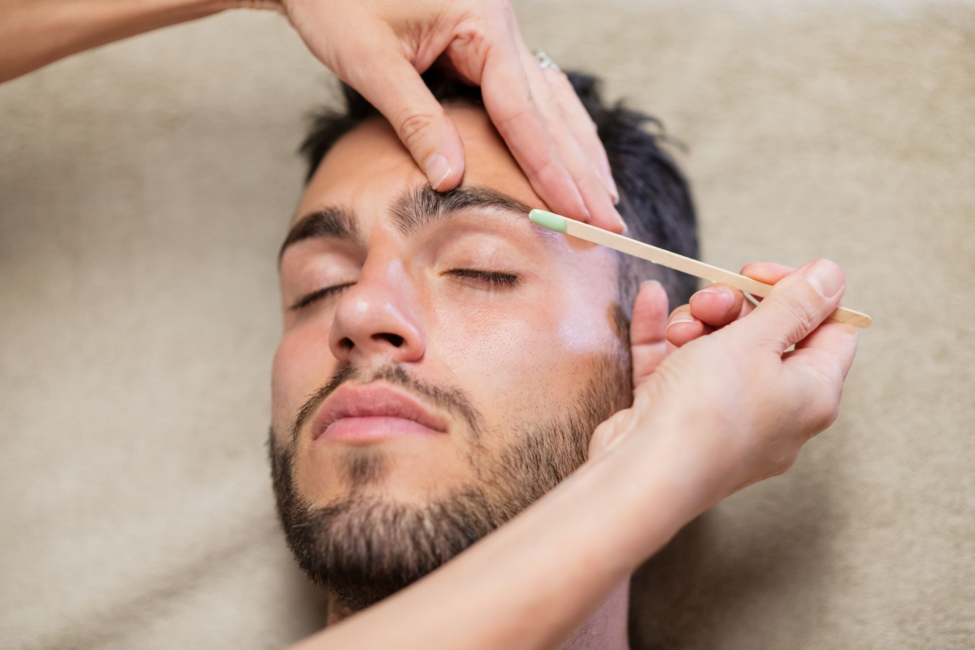 A man with a beard is getting his eyebrows waxed.