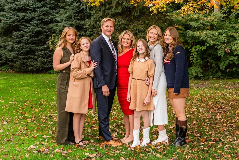 Six people posing outdoors on a lawn with autumn trees in the background