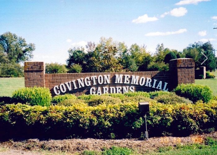 Covington Memorial Gardens sign amid green shrubs under a blue sky