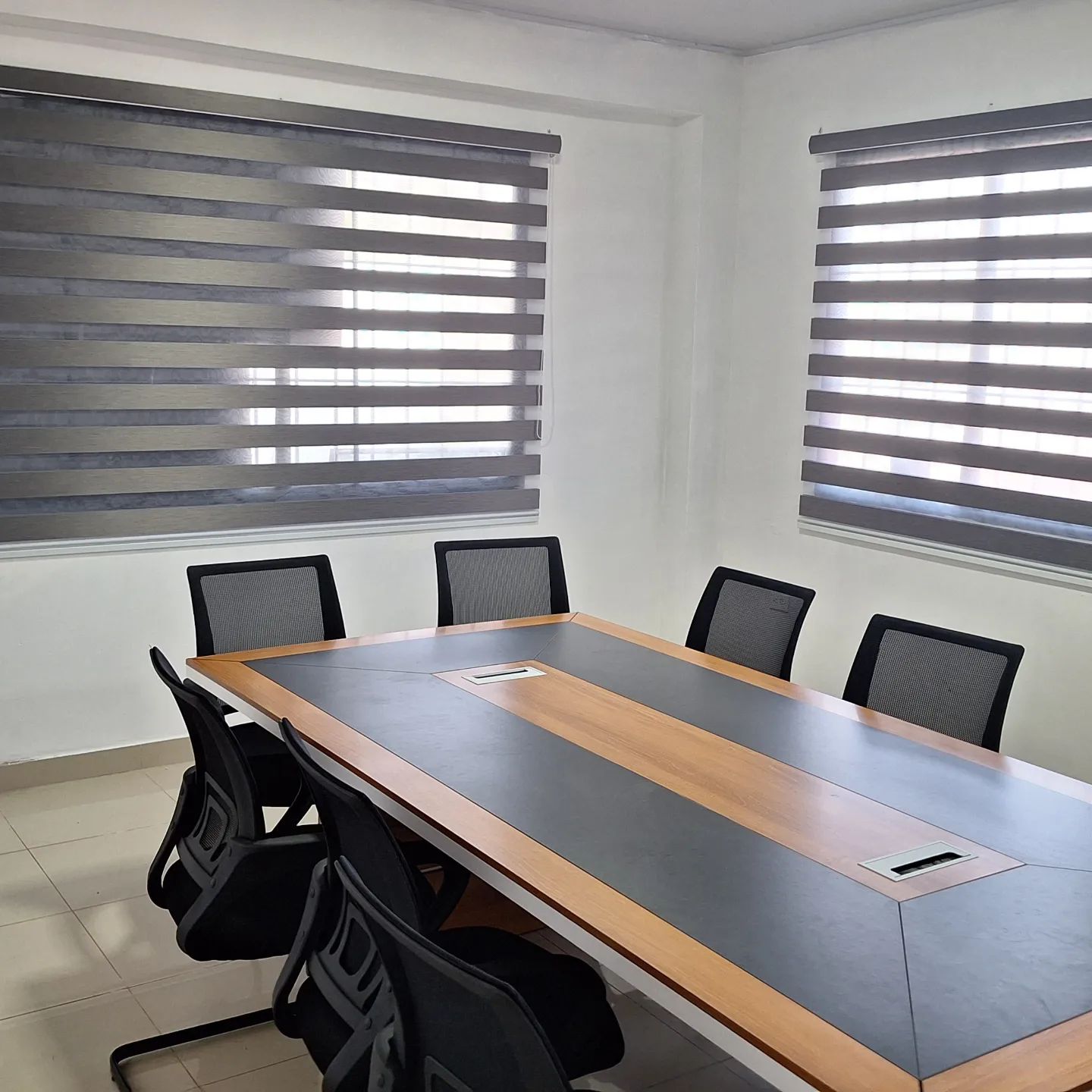 Sala de conferencias con una mesa larga de madera, sillas negras y cortinas rayadas.