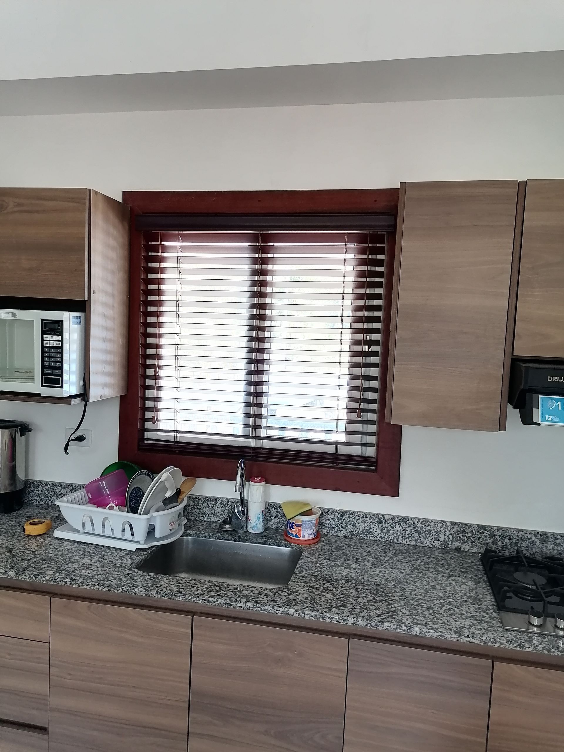 Cocina con gabinetes de madera, cubierta de granito, fregadero y ventana con persianas.